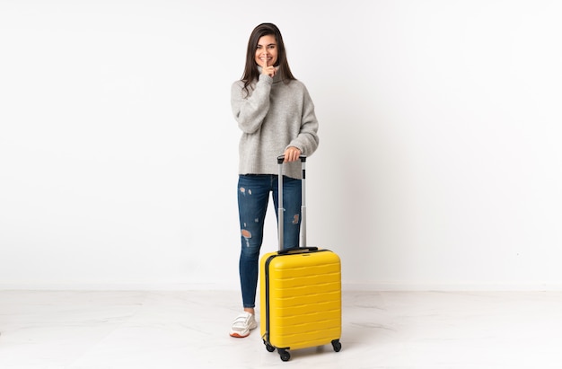 femme voyageur avec une valise sur mur blanc faisant le geste de silence