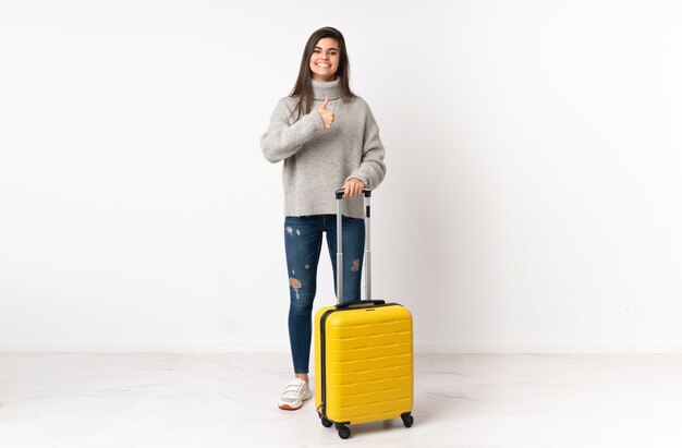 Femme de voyageur avec une valise sur un mur blanc isolé donnant un geste de pouce en l'air