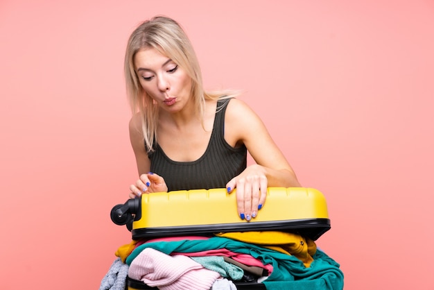 Femme voyageur avec une valise pleine de vêtements sur le mur rose isolé