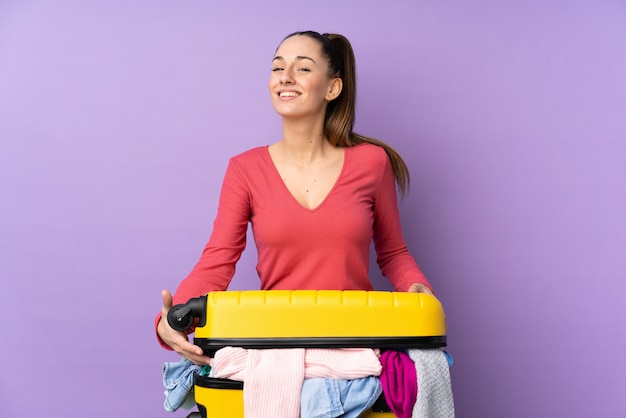 Femme voyageur avec une valise pleine de vêtements sur le mur violet isolé