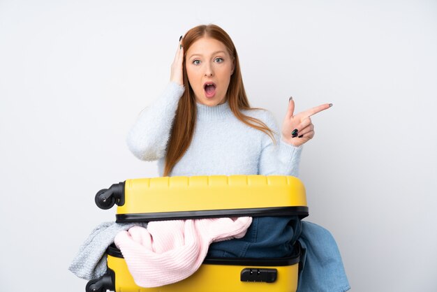 Femme de voyageur avec une valise pleine de vêtements surpris et pointant le doigt sur le côté