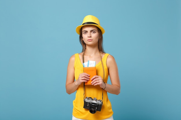 Femme de voyageur en vêtements décontractés d'été jaune et chapeau tenant une caméra de billets sur bleu