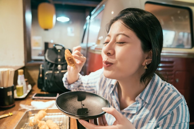 femme voyageuse aime manger de la nourriture japonaise à izakaya. jeune fille fermant les yeux tout en essayant de la nourriture délicieuse. expérience touristique style de vie nocturne japonais.