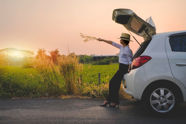 Femme voyageuse assise sur une voiture à hayon avec fond de montagne dans un ton vintage Dans la soirée, le soleil se couchait et elle tenait l'herbe dans sa main