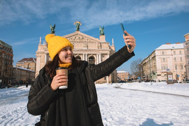 Femme voyageuse buvant du café pour aller prendre un selfie devant le bâtiment de l'opéra lviv city ukraine