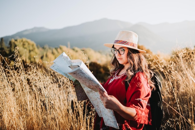 Femme voyageuse latine portant un chapeau, un poncho rouge et un sac à dos, vérifiant la carte pendant le trek