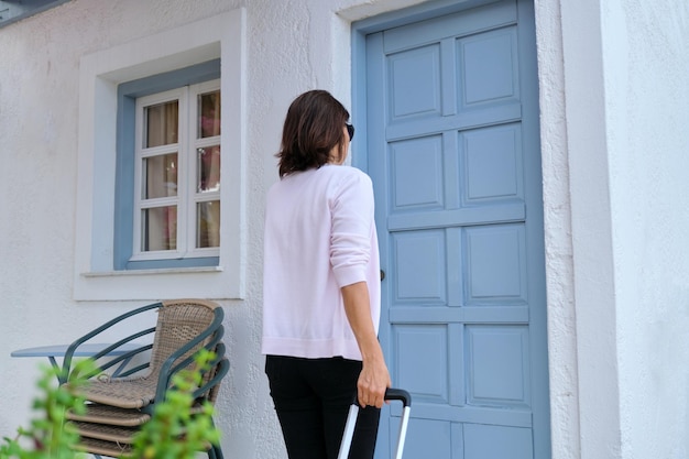 Femme voyageuse en plein air avec une valise jaune ouvrant la porte de fermeture de la maison