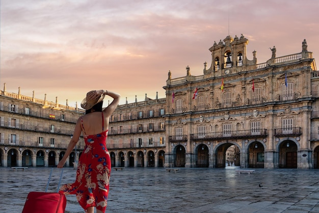 Photo femme voyageuse avec robe et valise rouge vient d'arriver à salamanque pour découvrir la ville et e