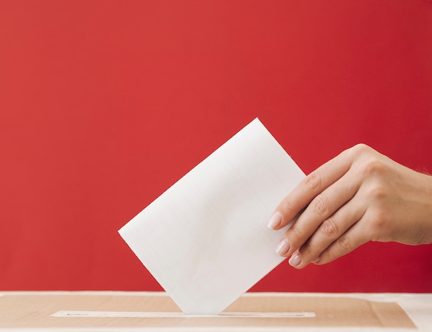 Femme vue de côté mettant un bulletin de vote dans une boîte avec un fond rouge