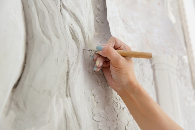 Une femme de workflow de réparation avec un outil ciseau sculpte un motif de bas-relief sur le mur