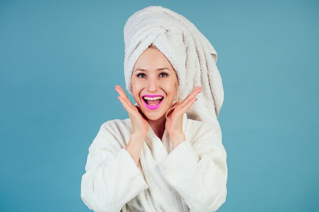 Femme wow séduisante et souriante, étonnée et choquée, vêtue d'un peignoir en coton blanc et d'un turban serviette sur la tête en studio sur fond bleu. concept de spa et fraîcheur hygiène féminine.