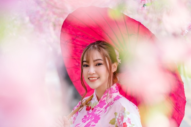 Femme en yukata (robe kimono) tenant un parapluie et à la fleur de sakura ou fleur de cerisier en fleurs dans le jardin