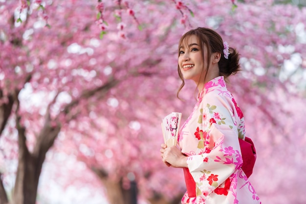 Femme en yukata (robe kimono) tenant un ventilateur pliant et à la fleur de sakura ou fleur de cerisier en fleurs dans le jardin
