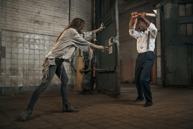 Une femme zombie se bat avec un homme effrayé dans une usine abandonnée. Horreur en ville, bestioles effrayantes, apocalypse apocalyptique, monstres diaboliques sanglants