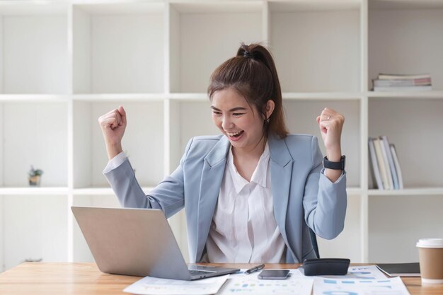 Photo des femmes d'affaires asiatiques montrent une expression joyeuse de succès au travail en souriant heureux avec un ordinateur portable dans un bureau moderne