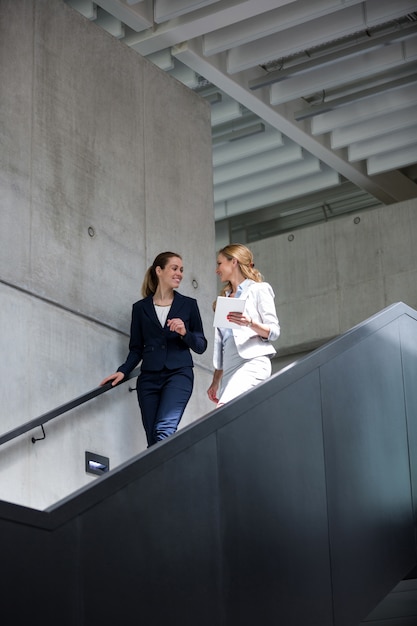 Femmes d'affaires discutant sur tablette numérique en marchant sur l'escalier