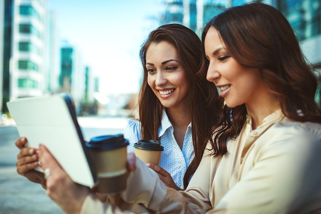 Les femmes d'affaires sont assises au parc de bureaux tout en utilisant une tablette numérique et en tenant une tasse de café jetable. L'équipe commerciale travaille ensemble en ligne tout en consultant.