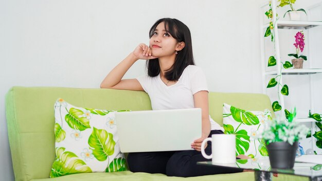 Les femmes asiatiques assis sur une chaise travaillent à domicile à l'ordinateur portable et réfléchissent à la solution du problème