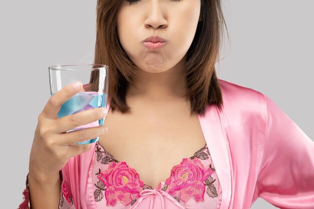 Photo des femmes asiatiques en chemise de nuit en satin et en robe rose se rincent et se gargouillent en utilisant un rince-bouche à partir d'un verre