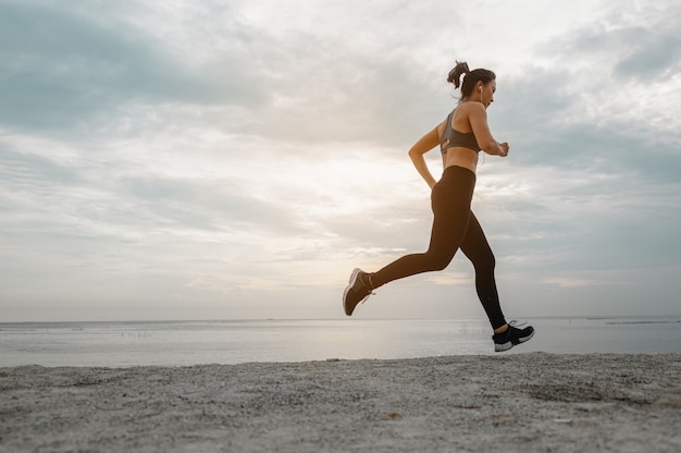 Femmes asiatiques faisant du jogging dans le sable sur la plage le matin. Exercice, remise en forme, entraînement, exercice de gym, mode de vie et concept sain.