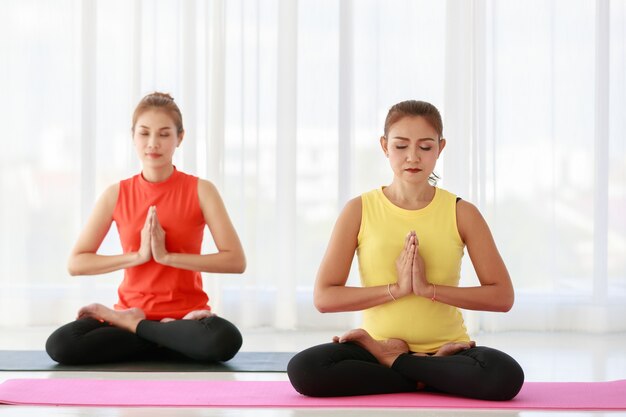 Femmes asiatiques fermant les yeux et serrant les mains tout en méditant dans la pose de Lotus pendant le studio de yoga