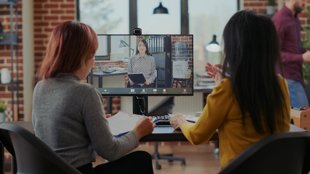 Des femmes asiatiques interrogent un candidat pour pourvoir un poste vacant par appel vidéo dans un bureau de démarrage. Les employés de l'entreprise rencontrent une femme pour embaucher un stagiaire sous contrat, en utilisant la vidéoconférence en ligne sur ordinateur.