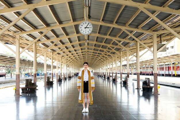 Les femmes asiatiques de la mode des années 20 portent une robe de manteau de luxe crème avec une ligne dorée. Jeune fille souriante et voyage en train à la gare ferroviaire en été