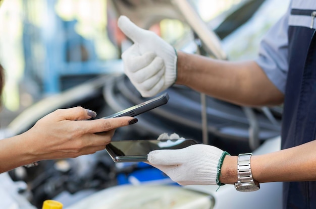 Photo les femmes asiatiques obtiennent des numéros de contact d'hommes mécaniciens automobiles asiatiques après avoir réparé le problème du moteur de la voiture et le scan de code qr pour payer le service de réparation et d'entretien de la voiture.