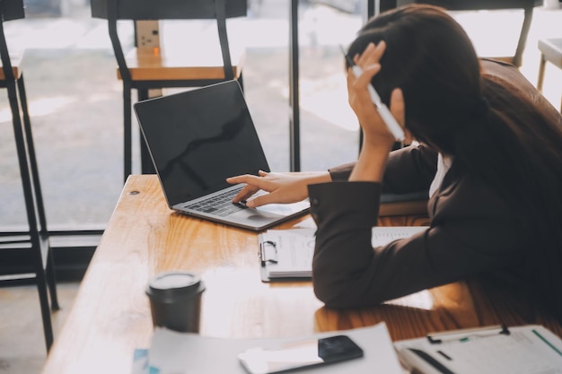 Les femmes asiatiques sont stressées en travaillant sur leur ordinateur portable. Une femme d'affaires asiatique fatiguée avec des maux de tête au bureau se sent malade au travail.