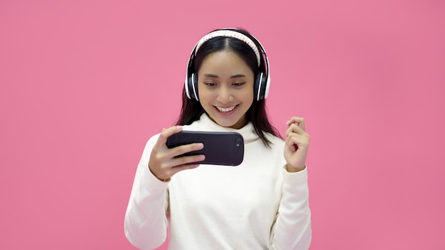 Femmes asiatiques souriant et écoutant et chantant la musique avec des écouteurs sur un fond de studio rose