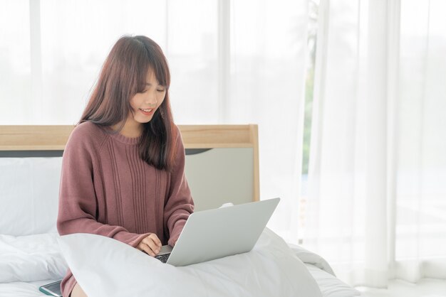 Femmes asiatiques travaillant avec un ordinateur portable sur le lit à la maison