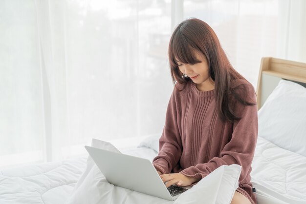 Femmes asiatiques travaillant avec un ordinateur portable sur le lit