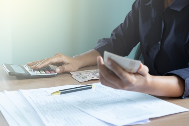 Femmes assises sur un bureau à l&#39;aide d&#39;une calculatrice et détenant de l&#39;argent