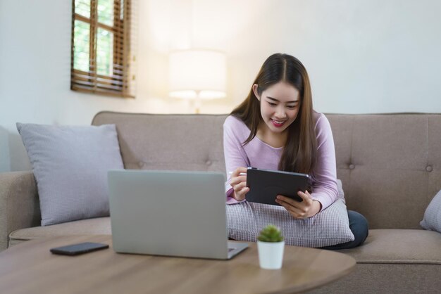 Des femmes assises sur un grand canapé et écrivant des notes sur une tablette et travaillant sur un ordinateur portable dans le style de vie à la maison