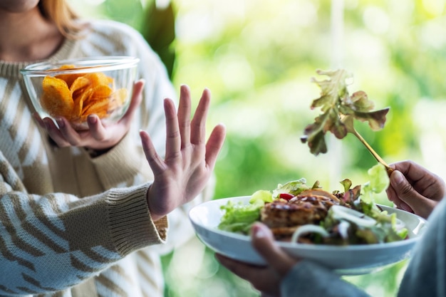 Photo femmes choisissant de manger des croustilles et faisant signe de la main pour refuser une salade de légumes