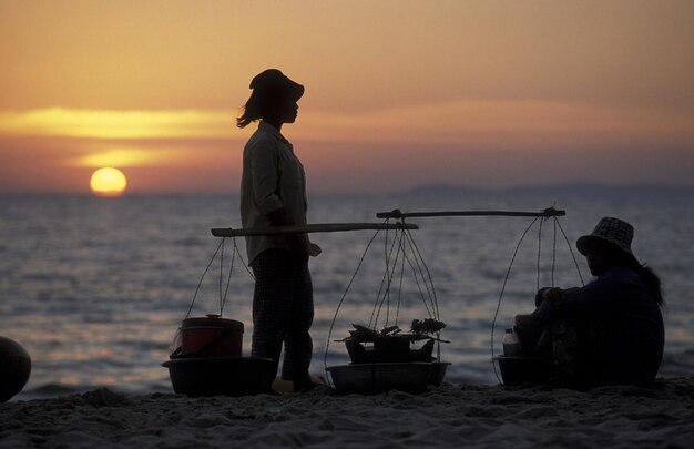 Photo des femmes avec des conteneurs reposant sur la plage contre le ciel au coucher du soleil