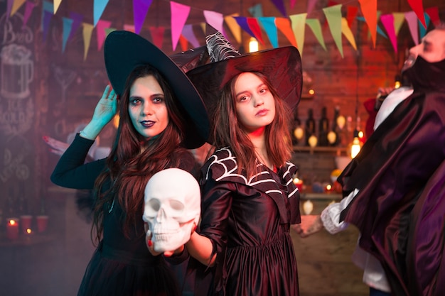 Femmes en costumes d'halloween debout avec un crâne humain à la main. Célébrer Halloween.