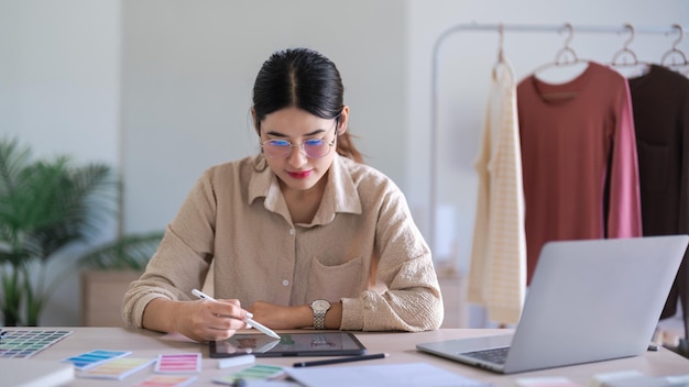 Les femmes de créateurs de mode travaillent à la conception de robes et à des croquis sur tablette pour une nouvelle collection créative