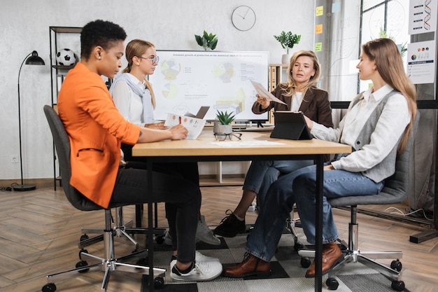 Des femmes économistes qualifiées assises au bureau avec une tablette pour ordinateur portable moderne et un grand écran