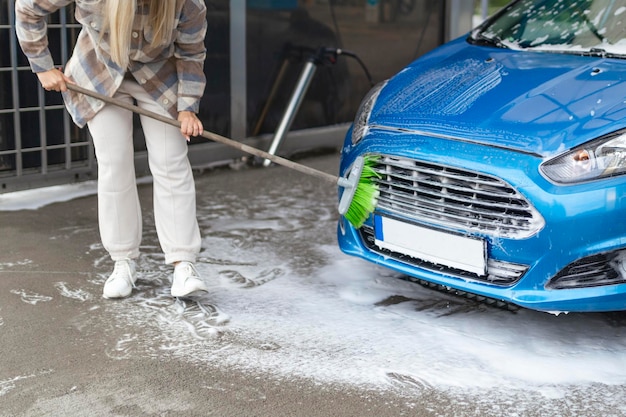 Les femmes elles-mêmes au lave-auto lave la voiture avec une brosse