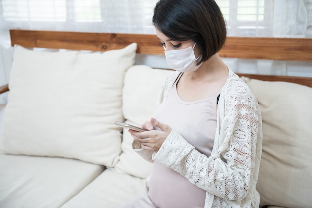 Les femmes enceintes asiatiques portant un masque médical en raison de la maladie, des étourdissements à l'aide d'un téléphone mobile intelligent avec inquiétude, le concept de soins de santé pandémique coronavirus (COVID-19).