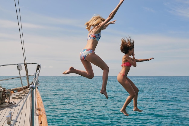 Des femmes enthousiastes sautant d'un bateau pour nager dans l'océan Des femmes joyeuses sautant d'un bateau pendant une croisière pour nager dans l'océan