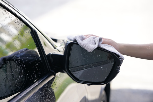 les femmes essuient à sec la surface de la voiture avec un chiffon microfibre après le lavage.