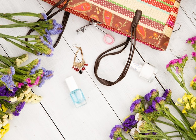 Photo femmes d'été sertie de sac de paille fleurs colorées cosmétiques maquillage bijou et essentiels sur fond en bois blanc