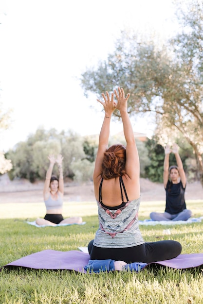 Femmes faisant des cours de yoga dans un parc extérieur avec leurs bras levés