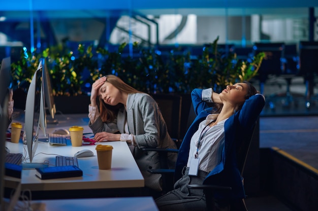 Les femmes fatiguées travaillent sur des ordinateurs au bureau de nuit