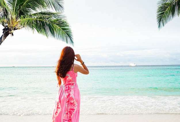 Femmes floues vêtues d'une robe rose debout seule sur la plage sous le cocotier