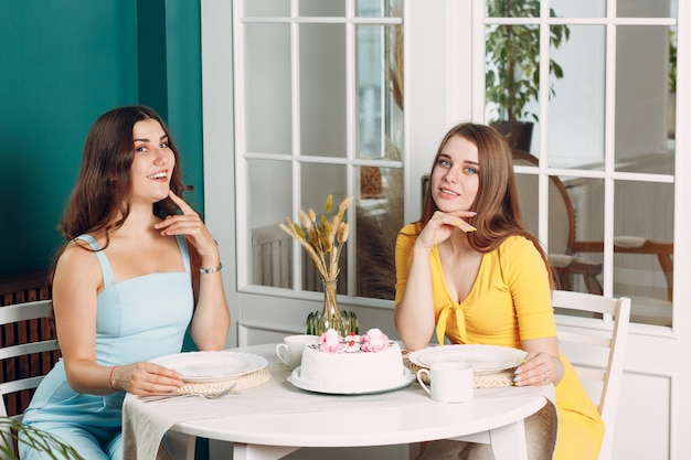 Femmes heureuses amies à la maison assises et souriantes avec un gâteau d'anniversaire blanc.