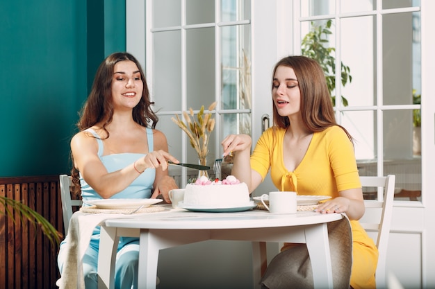 Femmes heureuses amies à la maison assises et souriantes avec un gâteau d'anniversaire blanc.