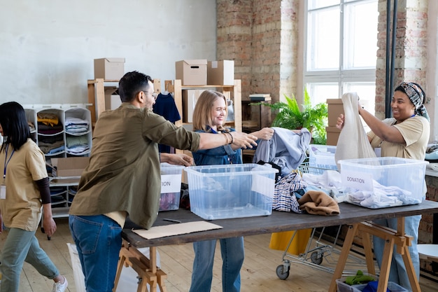 Femmes heureuses choisissant des vêtements de don dans des conteneurs sur une table